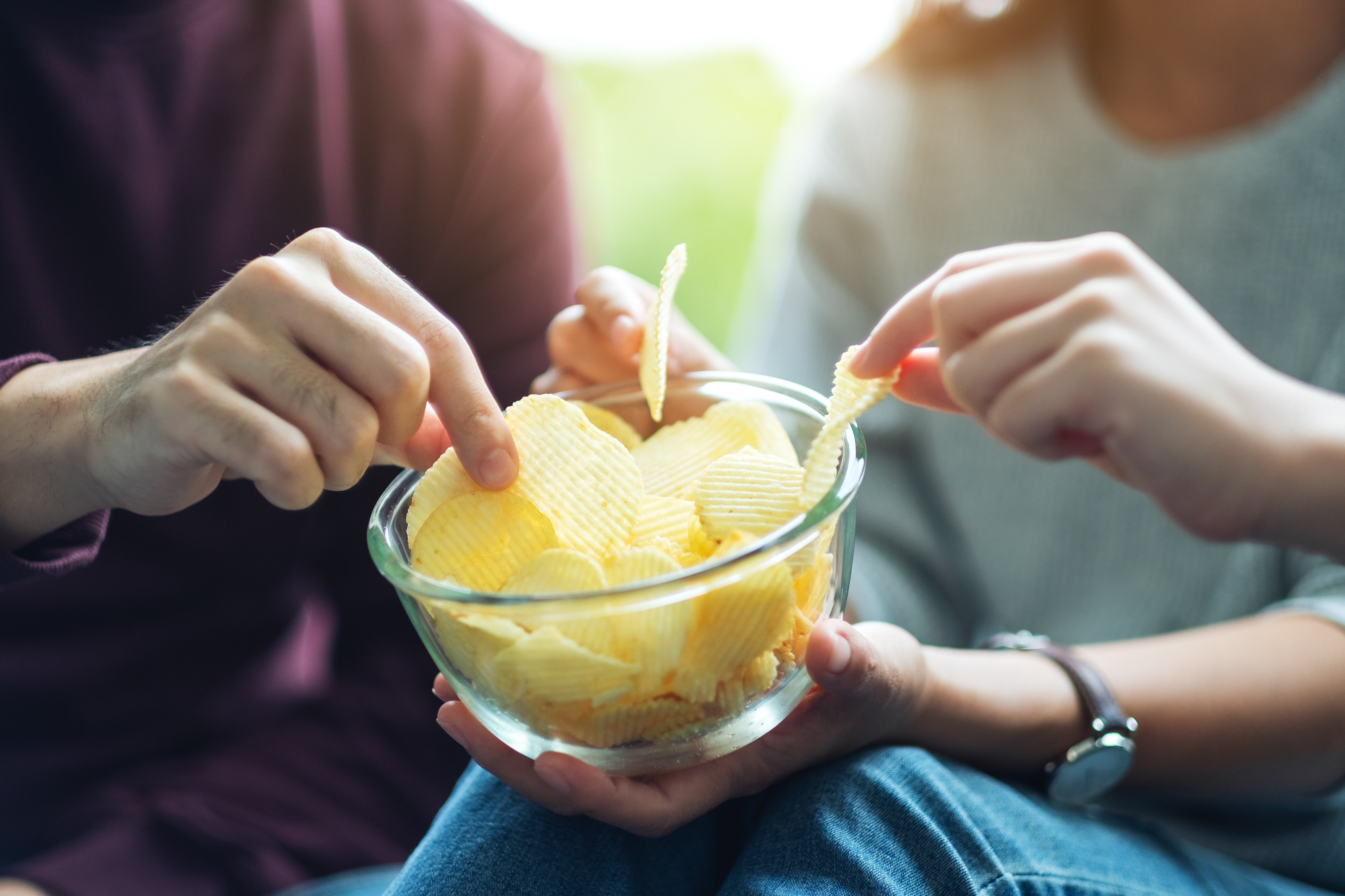 Closeup image of friends sharing and eating potato chips at home party together